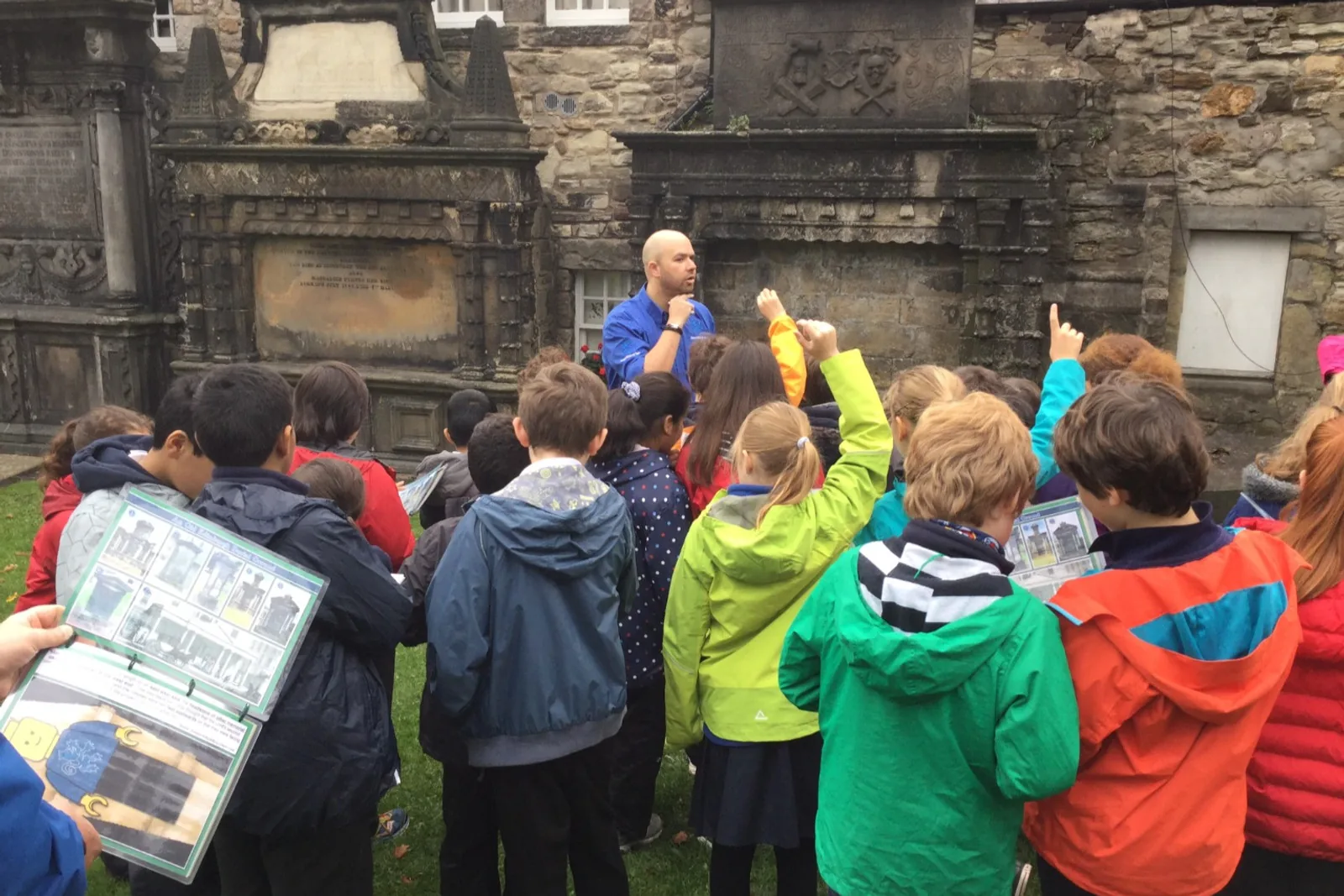 A primary school class working with clipboards in Greyfriars Kirkyard while their guide points something out